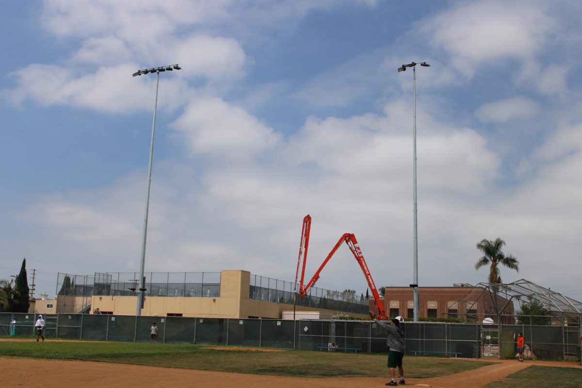 Newly installed lights rise above the baseball field, with the football field under construction behind the fence.