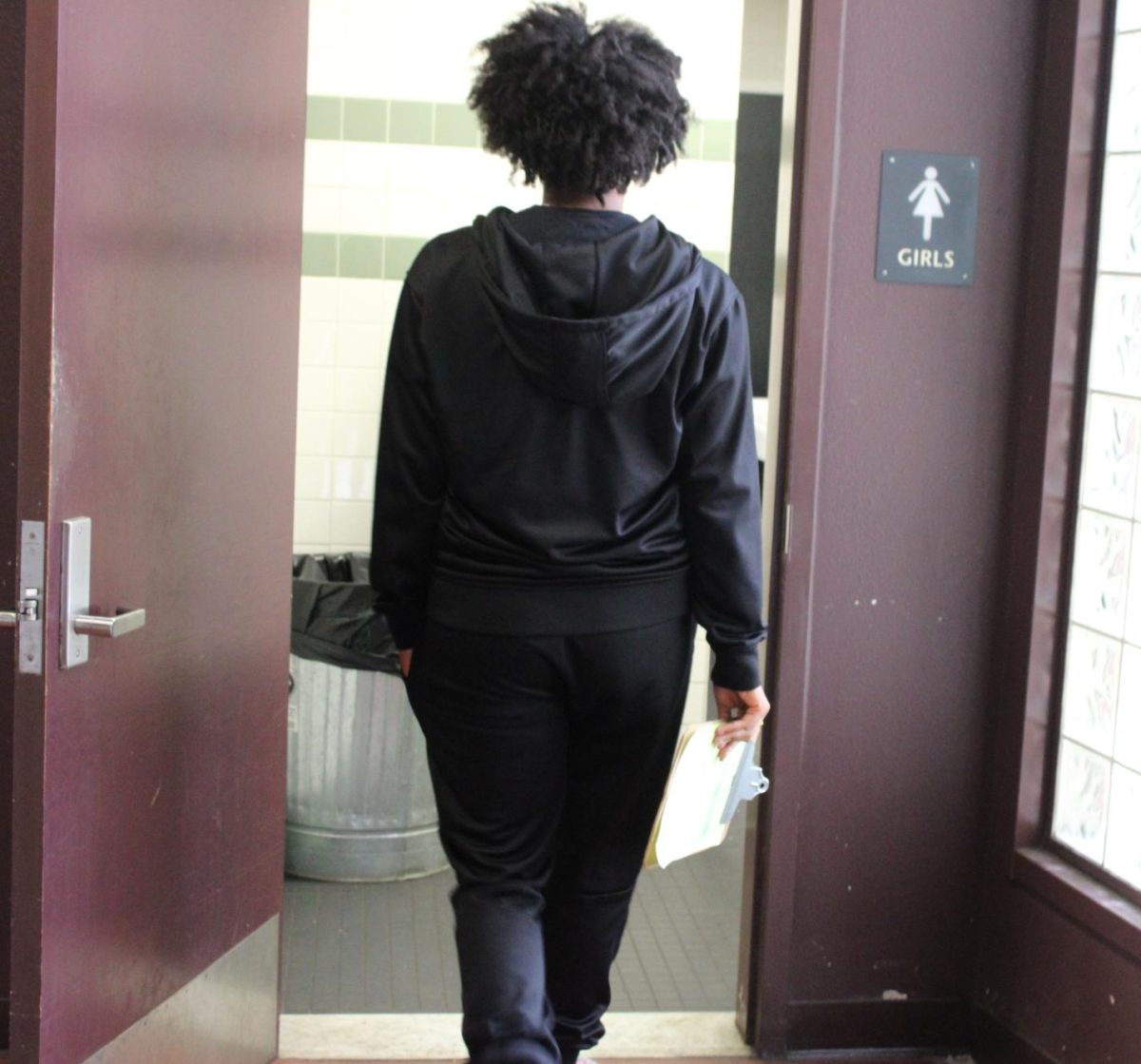 A student visibly holds their hall pass out as they go into the bathroom.