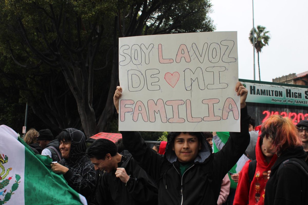 A student holds up a poster in Spanish that reads "I am the voice of my family."