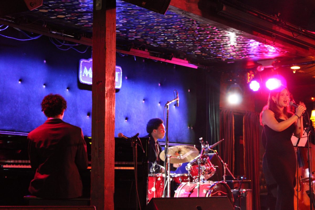 Olivia McNeill sings on stage, backed up by the music from students Mateo Arce and Victor Franklin.